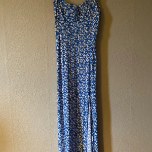 Blå blommig långklänning - Säljer en somrig blå långklänning med vita blommor. Klänningen har smala axelband och en fin slits framtill. Ställ gärna frågor!😊