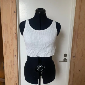 Vit ribbad linnetopp - Säljer en vit ribbad linnetopp med breda axelband. Toppen är croppad och har en enkel och stilren design. Perfekt för varma dagar eller som ett basplagg i garderoben.