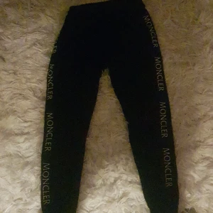Svarta leggings från Moncler - Snygga svarta leggings från Moncler med logotyp längs sidorna. Perfekta för en stilren och bekväm look. De är stretchiga och har en hög midja för extra komfort.