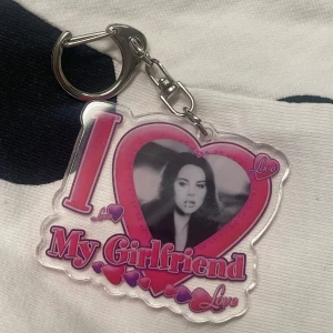 Nyckelring Lana del rey - En nyckelring med texten 'I Love My Girlfriend' i rosa och lila. Den har en bild i mitten omgiven av ett hjärta. Perfekt som en söt present eller för att visa uppskattning.