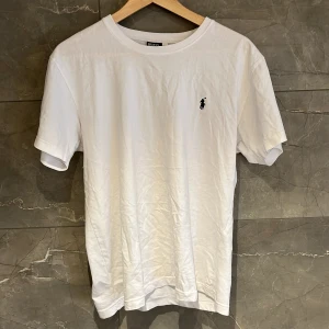 Vit t-shirt från Ralph Lauren - Säljer en klassisk vit t-shirt från Ralph Lauren med korta ärmar och en broderad logga på bröstet. Perfekt för en stilren och avslappnad look. Inga defekter alls skick 8,5/10. Är en L men sitter som en M passar bra på mig som är 179. 