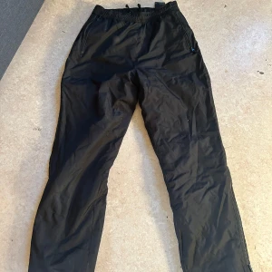 Svarta byxor med dragsko - Snygga svarta byxor med dragsko i midjan. Perfekta för en avslappnad stil. Byxorna har en rak passform och är tillverkade i ett lätt material. Drsgkedjor på benen