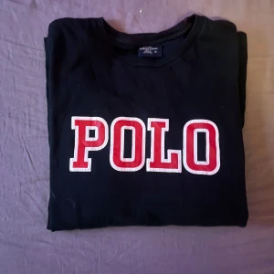 Svart långärmad tröja från Polo Ralph Lauren - Säljer en svart långärmad tröja från Polo Ralph Lauren med stor röd och vit POLO-text på framsidan. Tröjan är tillverkad i 100% bomull och har en klassisk rund halsringning. Perfekt för en stilren och avslappnad look. Tröjan är i ( S ) men passar även ( M )