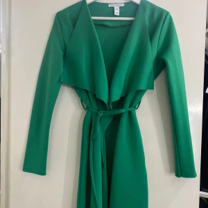 Grön långärmad trenchcoat med knytband - Snygg grön trenchcoat från nly trend med långa ärmar och ett elegant knytband i midjan. Perfekt för att ge en stilren look.