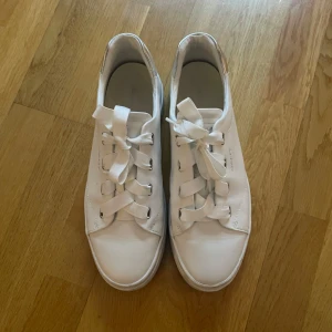 Vita sneakers från Gant - Snygga vita sneakers från Gant med breda snören och silverdetaljer vid hälen. Skorna har en stilren design med en tjock sula som ger extra komfort. Perfekta för en avslappnad och trendig look. Skorna är knappt använda utan bara sulan som tyder på användning men går att rengöra. 