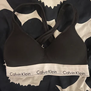 Svart linnetopp från Calvin Klein - Säljer en stilren svart linnetopp från Calvin Klein med vit resår och logga. Toppen har smala axelband och är perfekt för en avslappnad look. Passar bra till både jeans och kjol.