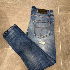Blå jeans med slitningar - Snygga blå jeans med slitningar och en klassisk femficksdesign. De har en normal passform och är perfekta för en avslappnad stil. Strl; 30/32 Jeansen har en dragkedja och knapp framtill. Modellen är 177 cm respektive 60kg. Mvh Sami