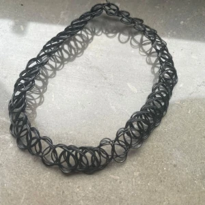 Svart elastiskt chokerhalsband - Säljer ett svart elastiskt chokerhalsband med ett klassiskt tatueringsmönster. Halsbandet är flexibelt och passar de flesta storlekar. Perfekt för att ge en edgy touch till din outfit.