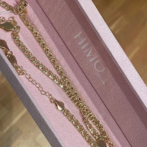 Guldhalsband med hjärtan från Himo - Elegant guldhalsband från Himo med fina hjärtformade detaljer. Halsbandet har en kedja med justerbar längd och är perfekt för att ge en stilfull touch till din outfit. Levereras i en rosa presentask.