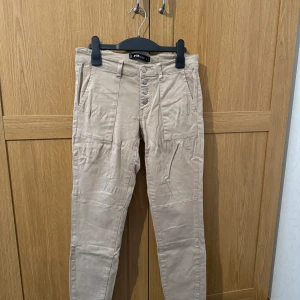 Beige byxor med knappar - Snygga beige byxor från FB Sisters med flera knappar framtill. Byxorna fickor både fram och bak. Ett par favoriter som inte sitter bra längre.