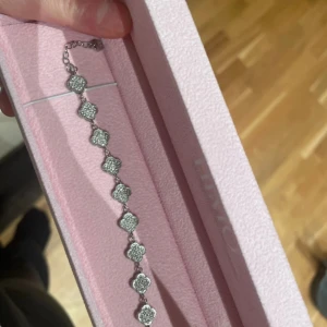 Silverfärgat armband med blommotiv - Elegant silverfärgat armband från Himo med blommotiv. Armbandet har en kedja med justerbar längd och blommor dekorerade med små stenar som ger en glittrig effekt. Perfekt för att lägga till en touch av glamour till din stil. Samt vattentåligt 