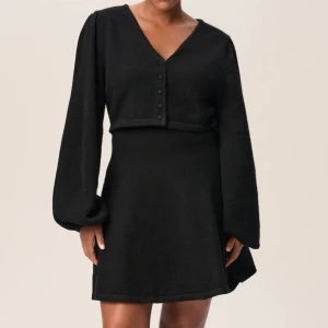 Svart klänning med v-ringning - Elegant svart klänning från Adoore med v-ringning och långa ärmar. Klänningen har en unik design med knappar framtill och en subtil öppning under bysten. Aldrig använd med prislapp kvar även 🤍.