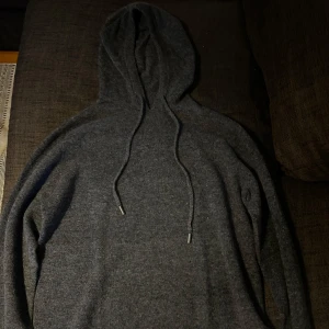Mörkgrå Merinoull hoodie - Säljer en stilren mörkgrå merinoull hoodie med långa ärmar och justerbar huva. Perfekt för kyliga dagar med sin mjuka och bekväma passform. Den har ribbade muddar vid ärmslut och nederkant för extra komfort. (Inget märke och inga lappar i tröjan)