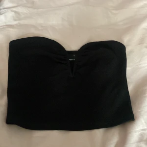 Svart tubtopp från Gina Tricot - Snygg svart tubtopp från Gina Tricot i en stilren design. Perfekt för att matcha med olika outfits. Toppen är axelbandslös och har en enkel och elegant look.