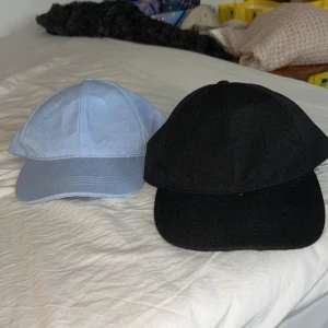 Svart och ljusblå keps - Två stilrena kepsar i svart och ljusblått. Justerbara remmar med metallspännen baktill för perfekt passform. De är aldrig använda. Priset är för båda.