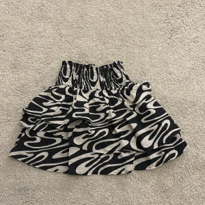 Svartvit kjol från H&M - Snygg svartvit kjol från H&M med ett unikt mönster och volangdetaljer. Kjolen har en elastisk midja för en bekväm passform. Perfekt för att ge din outfit en cool touch!