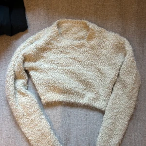 Beige/vit fluffig tröja - Säljer en supermjuk och fluffig beige tröja med lång ärm. Perfekt för kyliga dagar när du vill vara både varm och stilren. Tröjan har en croppad design som ger en modern touch. Passar perfekt till jeans eller kjol för en avslappnad look.