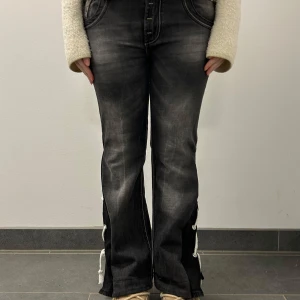 Svarta jeans med snörning från Frankie Malone - Coola svarta jeans från Frankie Malone med unik snörning på sidorna och en slitsdetalj. De har en klassisk femficksdesign och en snygg tvättad look. Perfekta för en trendig stil.