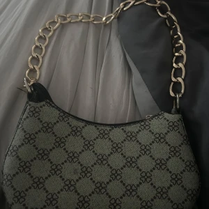 Mönstrad axelväska med kedja - Snygg axelväska med ett unikt mönster i svart och grönt. Väskan har en elegant kedja som axelrem och en stilren design. Perfekt för att ge din outfit en extra touch.