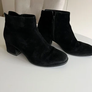 Svarta mocka boots med dragkedja - Snygga svarta boots i mocka med dragkedja på sidan. De har en bekväm klack och en stilren design som passar perfekt till olika outfits. Perfekta för höst och vinter.