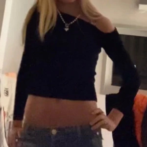 Svart offshoulder topp - Snygg svart offshoulder topp med långärmad design. Toppen är croppad och har en tight passform, perfekt för en trendig look. Passar bra till jeans eller kjol för en stilren outfit.