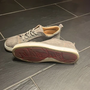 Gråa Christian Loubitin - Snygga grå sneakers med en unik röd sula och snörning. Skorna har en stilren design och en kontrasterande röd undersida som ger en cool touch. Skorna är i storlek 45.                                inga ob följer med!!!!!!
