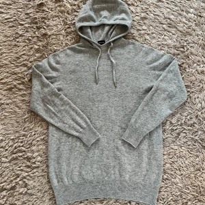 Grå cashmere hoodie från Vernando - Säljer en lyxig och mjuk grå hoodie från Vernando i 100% cashmere. Tröjan har en klassisk design med huva, och ribbade muddar. Perfekt för att hålla dig varm och stilren under kyliga dagar och perfekt till våren. Passa på att uppgradera din garderob med denna exklusiva tröja! Helt ny inte använd nån gång i storleken XS men passar även folk som har S
