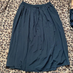 Svart långkjol med knytband - Elegant svart långkjol med knytband i midjan. Perfekt för en stilren look. Kjolen har en lös passform och är tillverkad i ett mjukt material som ger ett fint fall.