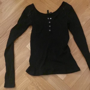 Svart ribbad tröja från Pieces - Säljer en svart ribbad tröja från Pieces med långa ärmar och dekorativa knappar framtill. Perfekt för en stilren look. Passar bra till både jeans och kjol.