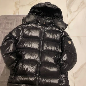 Moncler Maya - ⚜️Säljer en snygg svart pufferjacka från Moncler⚜️. ⚜️Jackan har en glansig finish och är perfekt för kalla dagar⚜️ Storlek 2 är det på jackan som motsvarar M men passar S beroende på passform ⚜️Den har en huva och långa ärmar, vilket gör den extra varm och skön⚜️. Perfekt för vintern! 🖤 Köpt för 4000kr, Mitt pris: 1799kr✨⚜️