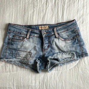 Blå jeansshorts med slitna detaljer - Så snygga blå jeansshorts med slitna detaljer och fransiga kanter. De har en låg midja och klassisk femficksdesign. Perfekta för en avslappnad sommarlook!