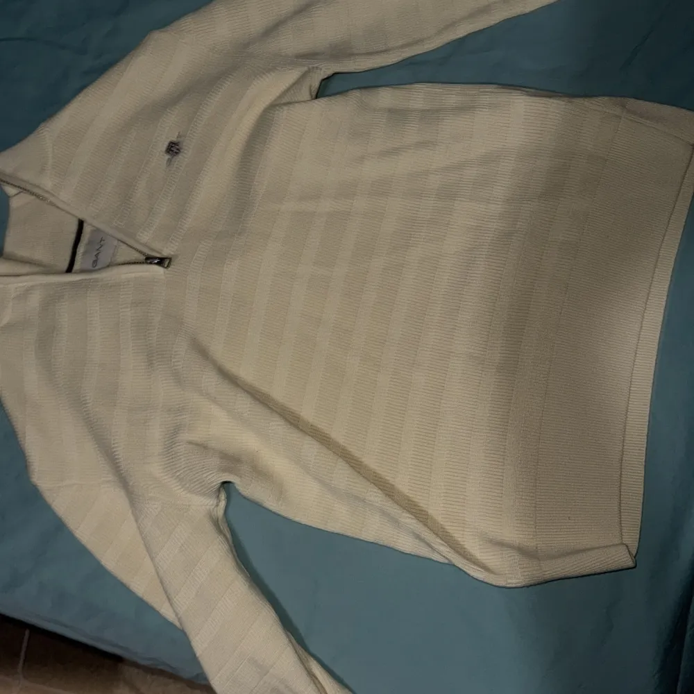 Säljer en stilren beige tröja från GANT i storlek S. Tröjan har en halv dragkedja framtill och är ribbad med ett diskret mönster. Perfekt för en avslappnad och snygg look. Använd en gång!!!. Neuletakit & Villapaidat.