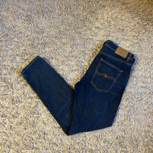 Mörkblå jeans från Nudie modell lean Dean  - Snygga blå jeans från Nudie Jeans med klassisk femficksdesign och orange sömmar. Jeansen har en slim/straight passform och är tillverkade i bomull. Perfekta för en avslappnad stil. Modell Lean Dean strlk 32/30, inga märkvärda anmärkningar. Fraktas antigen samma dag som köp eller dagen därpå, sänker priset 50kr vid snabb och smidig affär 🙌💯