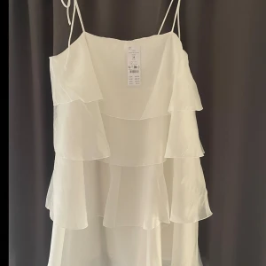 Vit klänning med volanger - En vit klänning från Gina i storlek 38