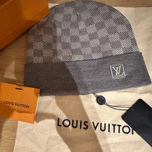 Grå rutig mössa  - Snygg grå mössa med ett klassiskt rutigt mönster. Mössan har en uppvikt kant och en diskret logotyp framtill. Perfekt för att hålla stilen i kallare väder.ÄKTA MÖSSA JUST NU 699kr 