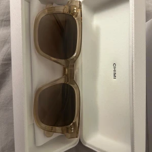 Chimi glasögon  - Snygga transparenta solglasögon från Chimi med fyrkantig form. De har en stilren design och kommer i ett elegant vitt fodral. Perfekta för att ge din stil en modern touch.