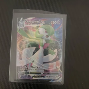 Gardevoir VMAX Pokémonkort - Säljer ett Gardevoir VMAX Pokémonkort med 320 HP. Kortet har en färgglad design med Gardevoir i fokus och inkluderar attacken Max Cure. Perfekt för samlare eller spelare som vill stärka sin kortlek.