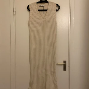 Beige ribbad klänning från Zara - Snygg beige ribbad klänning från Zara i ärmlös design. Den har en v-ringad hals och är perfekt för en stilren look. Klänningen är i en mjuk och bekväm polyesterblandning.