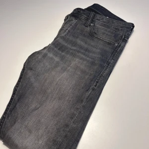 Grå jeans från Jack & Jones - Snygga grå jeans från Jack & Jones i modellen Slim Glenn. De har en slim passform och klassisk femficksdesign med knapp och dragkedja. Perfekta för en stilren look! 