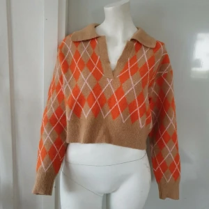 Beige och orange argyle-mönstrad tröja - Säljer en snygg och trendig beige och orange tröja med argyle-mönster. Tröjan är croppad med långa ärmar och en klassisk krage. Perfekt för en stilren och avslappnad look. 🌟 Har i storlek S och M