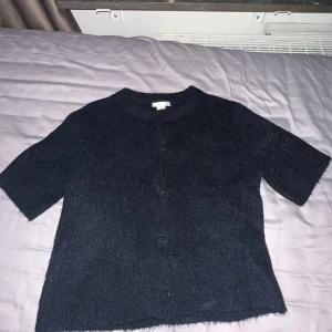 Mörkblå stickad kofta från Gina Tricot - Säljer en mörkblå stickad kofta från Gina Tricot. Koftan har korta ärmar och knappar framtill. Perfekt för en stilren och bekväm look. Passar bra till både jeans och kjol. Aldrig använd