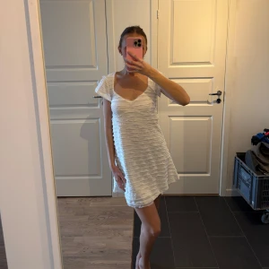 Vit kortklänning med volangdetaljer - Säljer en söt vit kortklänning med volangdetaljer. Klänningen har en v-ringad hals och korta ärmar, perfekt för sommarens varma dagar. Den är gjord i ett lätt och luftigt material som ger en skön passform.