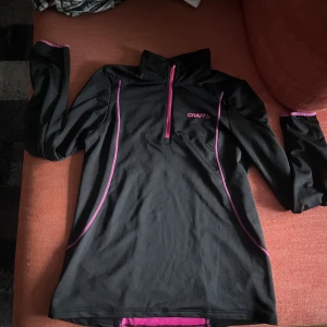 Svart och rosa tröja från Craft - Säljer en svart tröja från Craft med rosa detaljer och dragkedja. Tröjan har långa ärmar och en hög krage, perfekt för träning eller löpning. Den är designad för att ge en bekväm passform och har en snygg rosa panel på baksidan. Är i storlek L men sitter som S/M.🖤