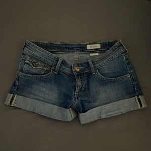 Jeansshorts med uppvikta ben - Snygga jeansshorts i blå denim med uppvikta ben och klassisk femficksdesign. Perfekta för en avslappnad stil. De har en knapp och dragkedja framtill samt dekorativa sömmar på bakfickorna.