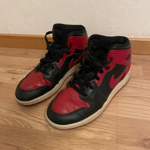 Nike Air Jordans i svart och rött - Säljer ett par klassiska Nike Air Jordans i svart och rött. Skorna har en ikonisk design med snörning och en hög siluett. Perfekta för sneaker-entusiaster som vill ha en tidlös stil. Den är lite sliten där bak men man tänker inte på det. 