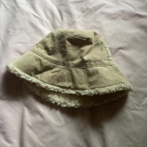 Beige bucket hat med teddyfoder - Säljer en mysig beige bucket hat med teddyfoder. Hatten har en mjuk och fluffig insida som håller dig varm under kyliga dagar. Perfekt för höst och vinter!