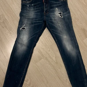 Blå jeans från DSQUARED2 - Snygga blå jeans från DSQUARED2 med slitna detaljer och en cool tvätt. De har en klassisk femficksdesign och en röd etikett med logotypen på baksidan. Perfekta för en avslappnad stil.