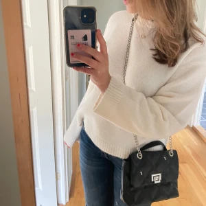 Svart axelväska med kedjedetalj - Snygg svart axelväska med silverfärgad kedja och spänne framtill. Perfekt för att bära dina nödvändigheter med stil. Väskan har en modern design som passar till många olika outfits.