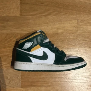 Nike Air Jordans i grönt och vitt - Snygga Nike Air Jordans i grönt och vitt med gula detaljer. Skorna har klassisk snörning och en ikonisk design med perforerad tå för extra ventilation. Skick: 8/10