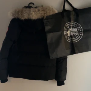 Svart dunjacka från Canada Goose - Säljer en svart dunjacka från Canada Goose med pälskantad huva. Jackan har en klassisk design med långärmade ärmar och en varm, quiltad insida. Perfekt för kalla vinterdagar. 🖤har även garanti kortet kvar och massa andra tillbehör till jackan🖤